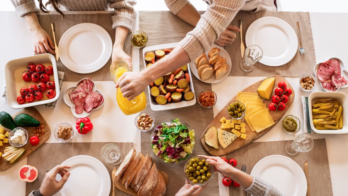 Aerial shot of a diverse brunch spread on a table with multiple hands serving food.